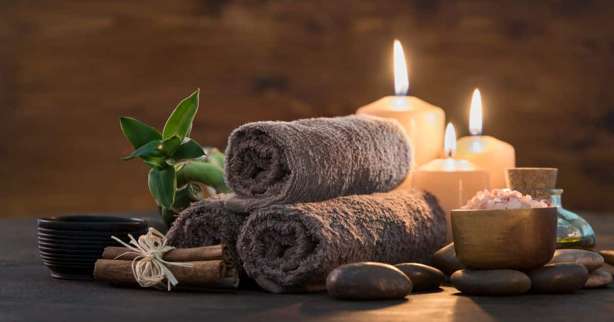Three candles burning behind three brown rolled up face towels