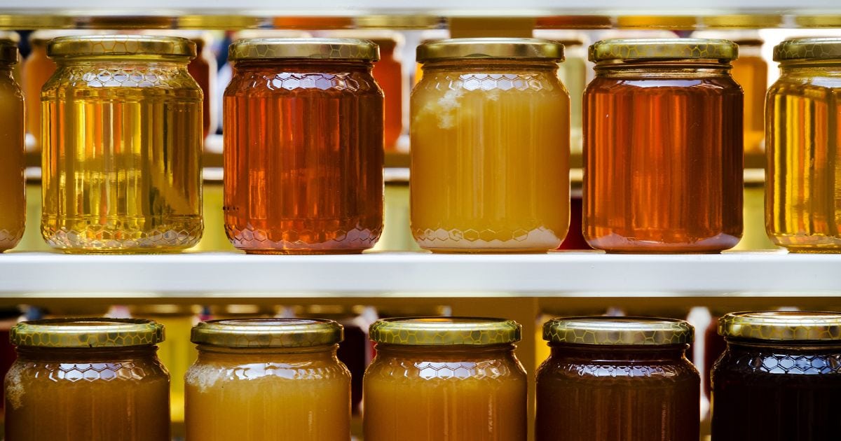 Two white shelves full of jars of different types and colours of honey